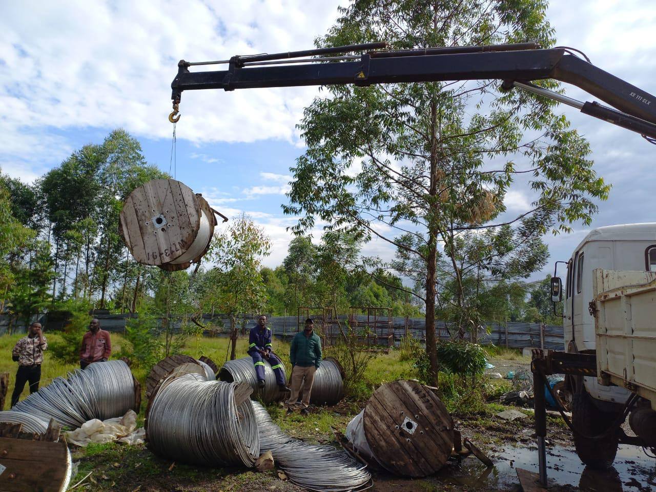 Crane truck offloading drums of overhead conductor cable at a power project yard