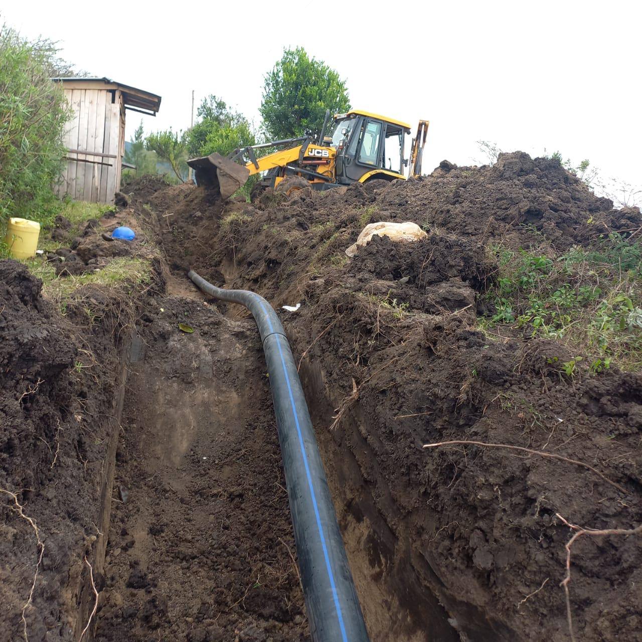 Backhoe excavating a trench for an HDPE water pipeline in rural Kenya